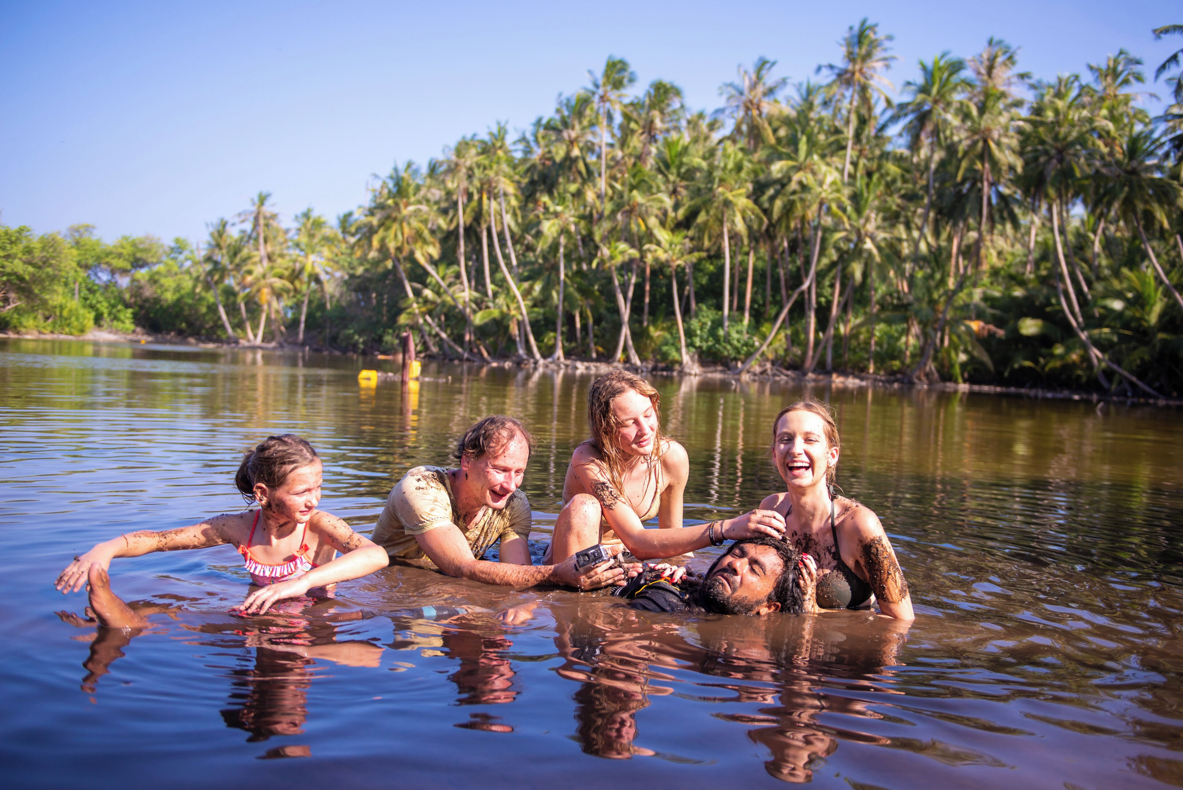 Um grupo de pessoas em um ambiente aquático natural, com palmeiras ao fundo.