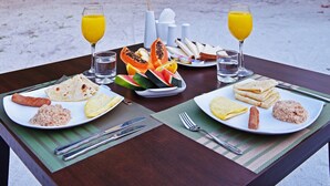 Ein Tisch mit Frühstücksangeboten, darunter Eier, Toast und Obst, vor einer Kulisse aus üppiger Vegetation und Palmen.