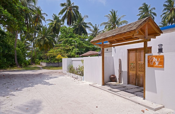 Ein Strandgrundstück mit einer Holzpergola, einer weißen Wand mit einer Holztür und einem Schild mit der Aufschrift 'ASAA VIEW'.