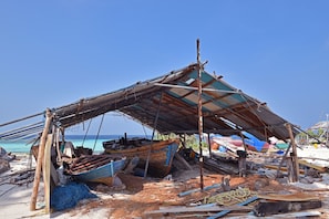 Ein Strand mit einer provisorischen Schutzhütte, Holztrümmern und einem teilweise versunkenen Boot.