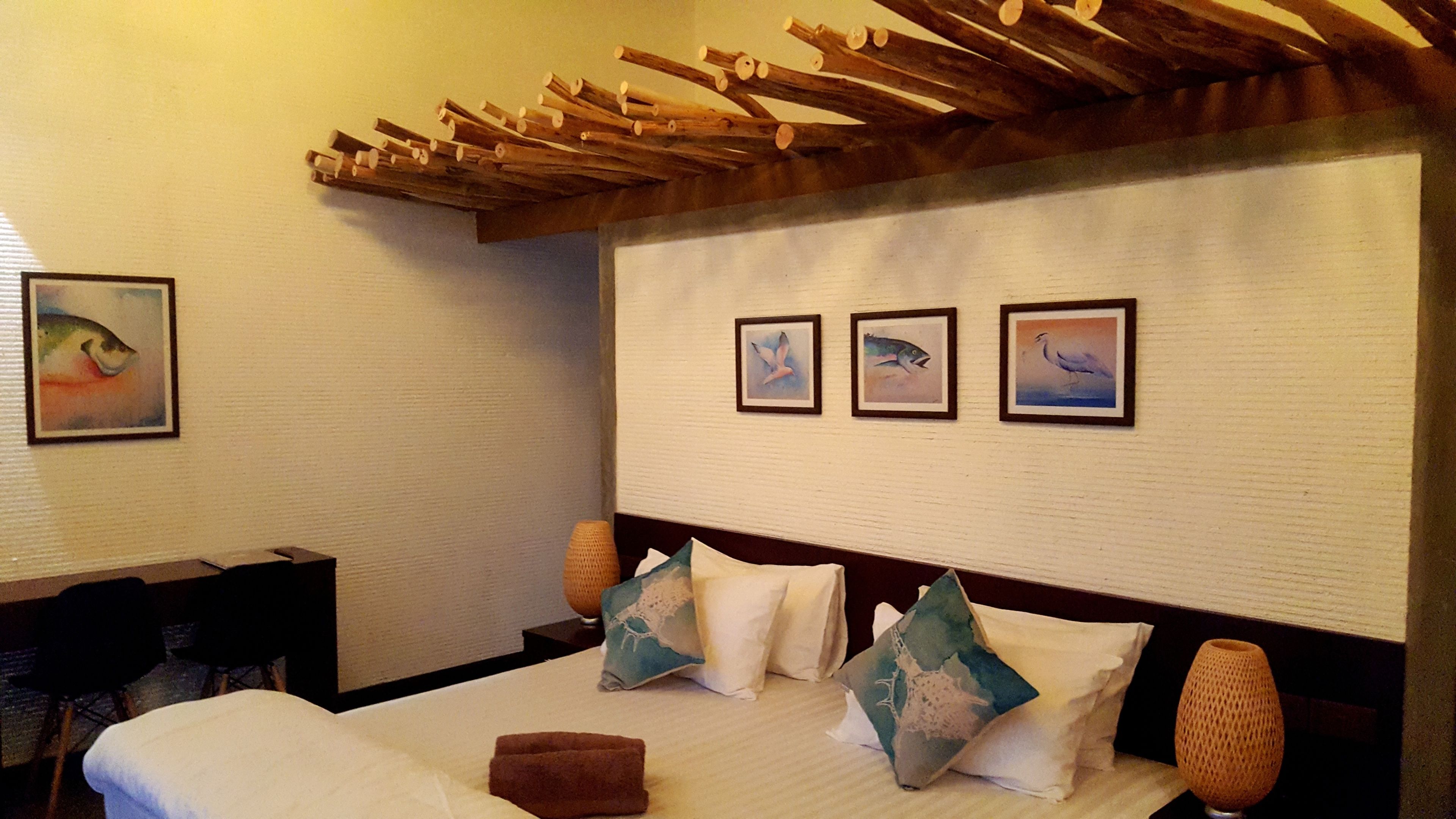 A hotel room with a bed, pillows, a wooden ceiling, and three framed pictures on the wall.