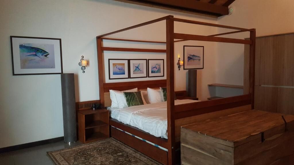 Una cama con dosel de madera, una mesita de noche y una mesilla auxiliar. Hay cuadros enmarcados en la pared sobre la cama.