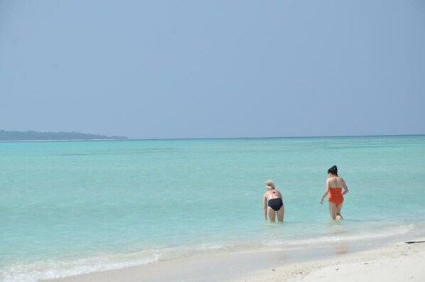 Two people walking on a beach with clear turquoise water.