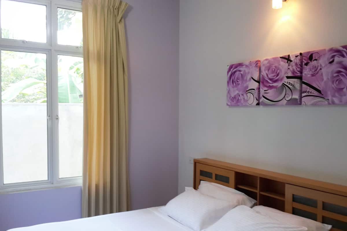 A bedroom with a bed, a window with curtains, and a wall-mounted artwork.