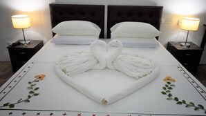 Cama bem arrumada com toalhas dispostas em formato de coração e cisnes, acompanhadas por mesas de cabeceira com abajures, em um quarto de hotel.