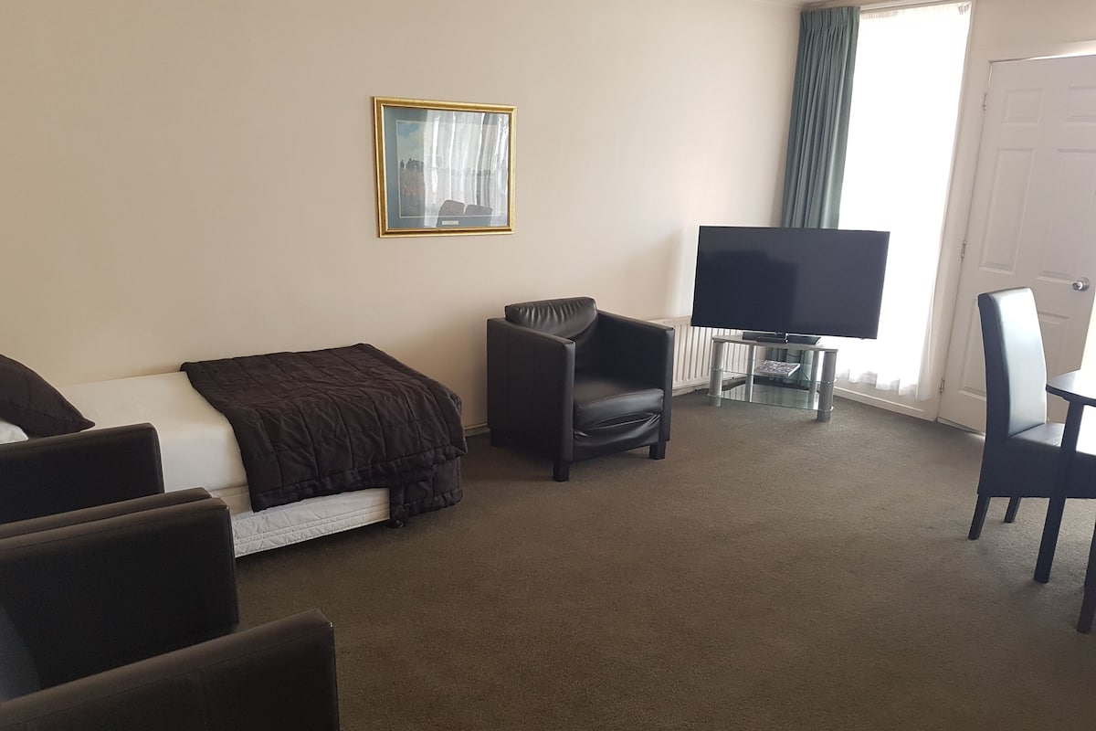 A hotel room with a bed, a chair, a TV, and a window with curtains.