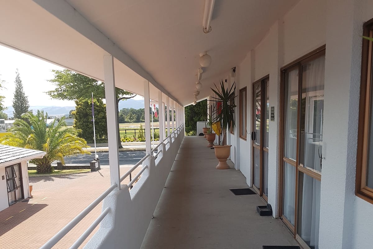 A covered corridor with potted plants, a railing, and a view of the outdoors.