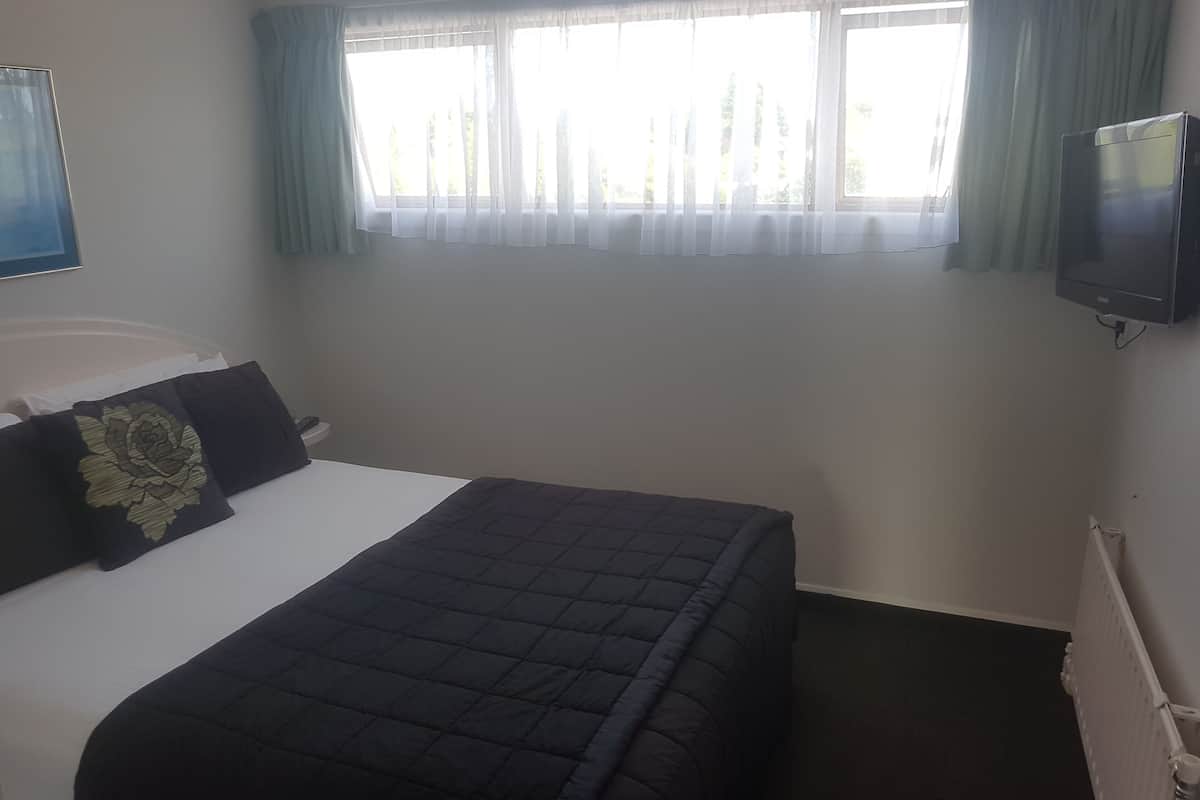 A hotel room with a bed, a television mounted on the wall, and a window with curtains.