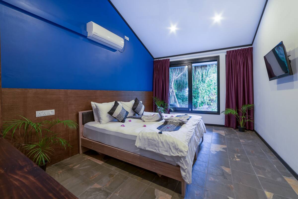 Une chambre à coucher avec un lit, une fenêtre avec des rideaux, un climatiseur fixé au mur et un téléviseur mural.