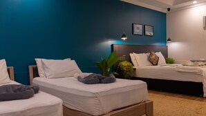 Habitación de hotel con dos camas individuales, una cama grande y una mesita pequeña.