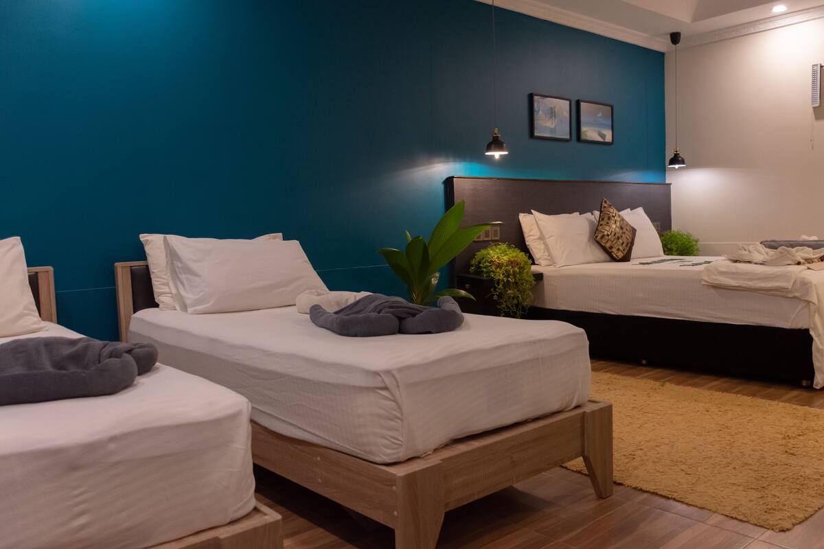 Une chambre d’hôtel avec deux lits simples, un grand lit et une petite table.