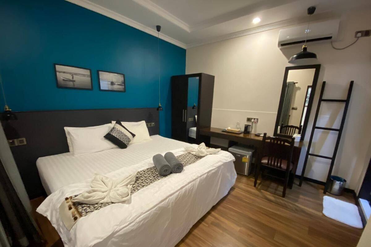 Un lit bien fait, avec du linge de lit blanc, un mur d’accent bleu, un plancher en bois, un bureau avec une chaise et un miroir.