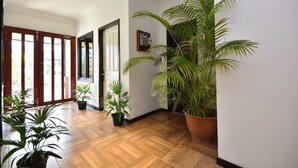 Un pasillo con suelo de madera, plantas en macetas y una puerta que da a un espacio al aire libre.