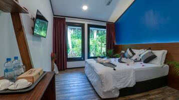 Quarto com cama, escrivaninha com objetos sobre uma bandeja, televisão na parede e janela com cortinas.