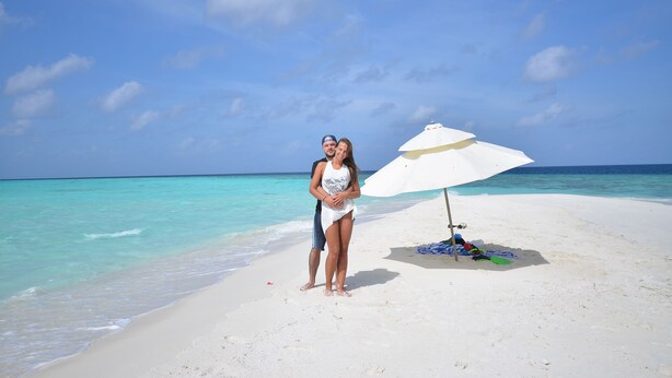 A couple standing on a beach with a white umbrella and a beach chair. - Holiday Haven Ukulhas (Ukulhas)
