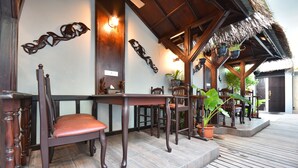 A wooden outdoor seating area with a table and chairs, a thatched roof, and decorative wall art. - Holiday Haven Ukulhas (Ukulhas)