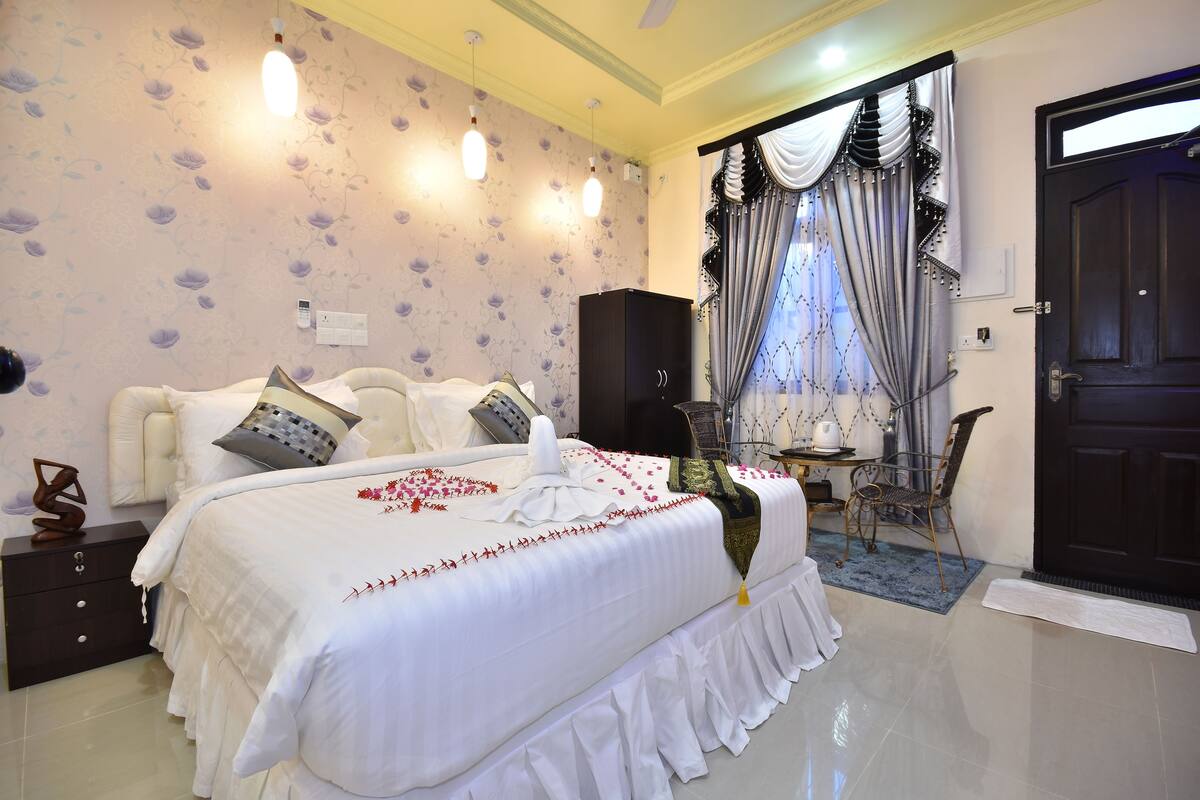 Un dormitorio ordenado con una cama grande, una mesita de noche, un armario y una ventana con cortinas.