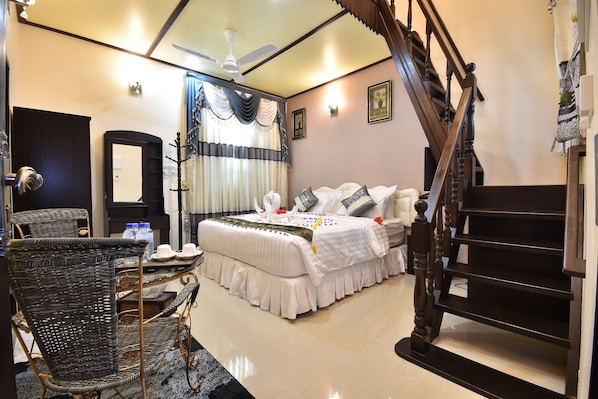 A bedroom with a bed, a chair, a table, a mirror, a ceiling fan, and a staircase. - Holiday Haven Ukulhas (Ukulhas)
