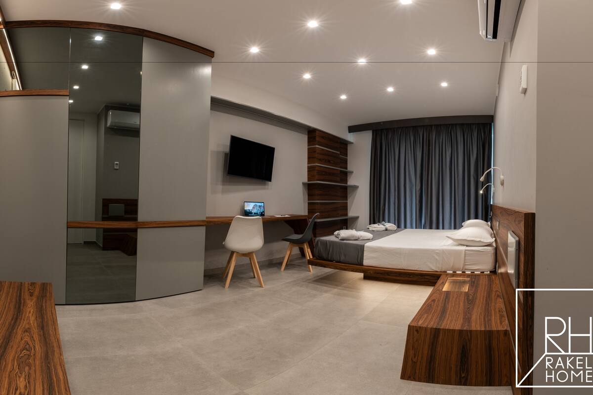 Ein modernes Hotelzimmer mit einer gebogenen Schreibtischplatte, einem Bett, einem Fernseher und einer Duschkabine.
