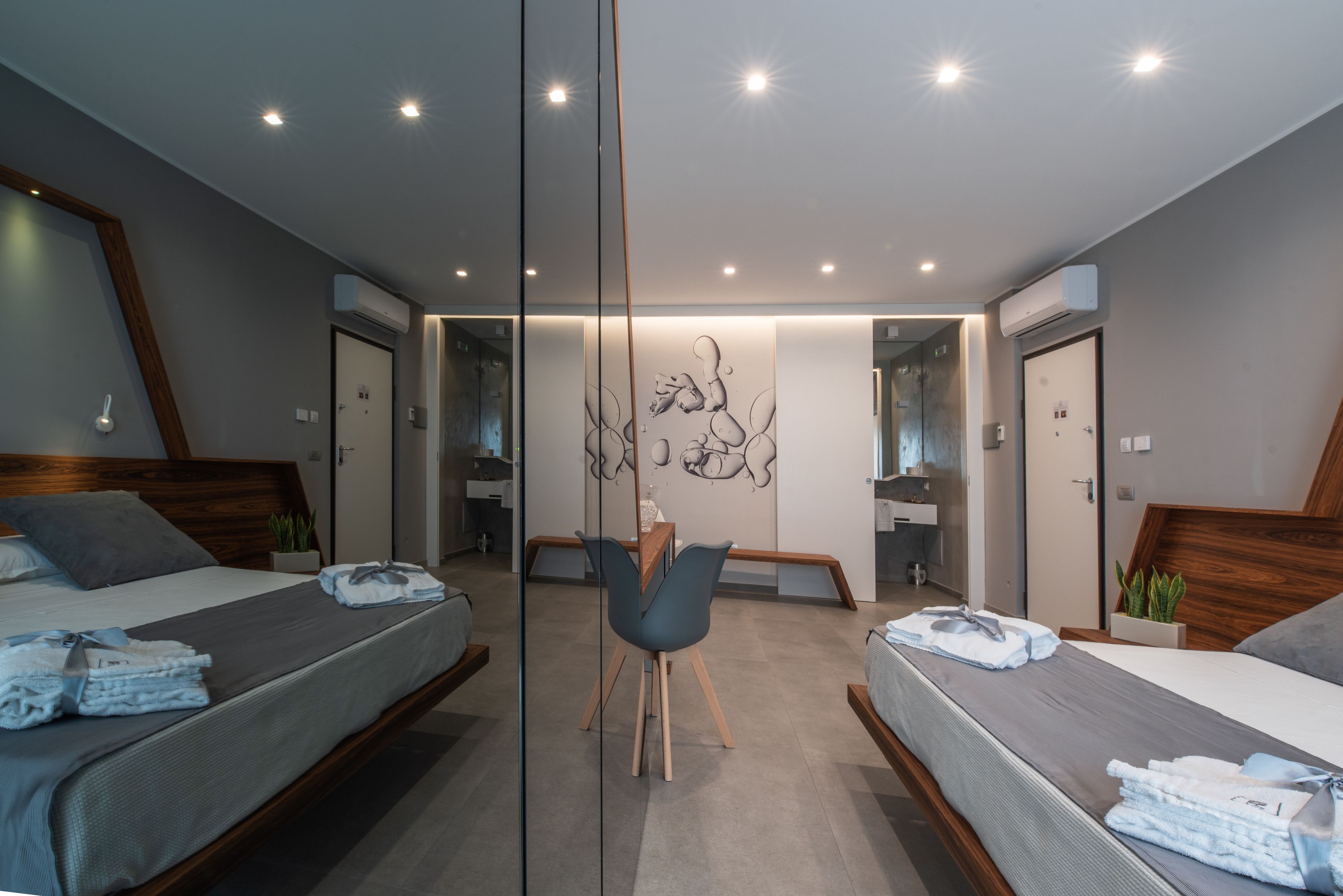 Una habitación de hotel moderna con dos camas, un espejo grande y una zona de estar central.