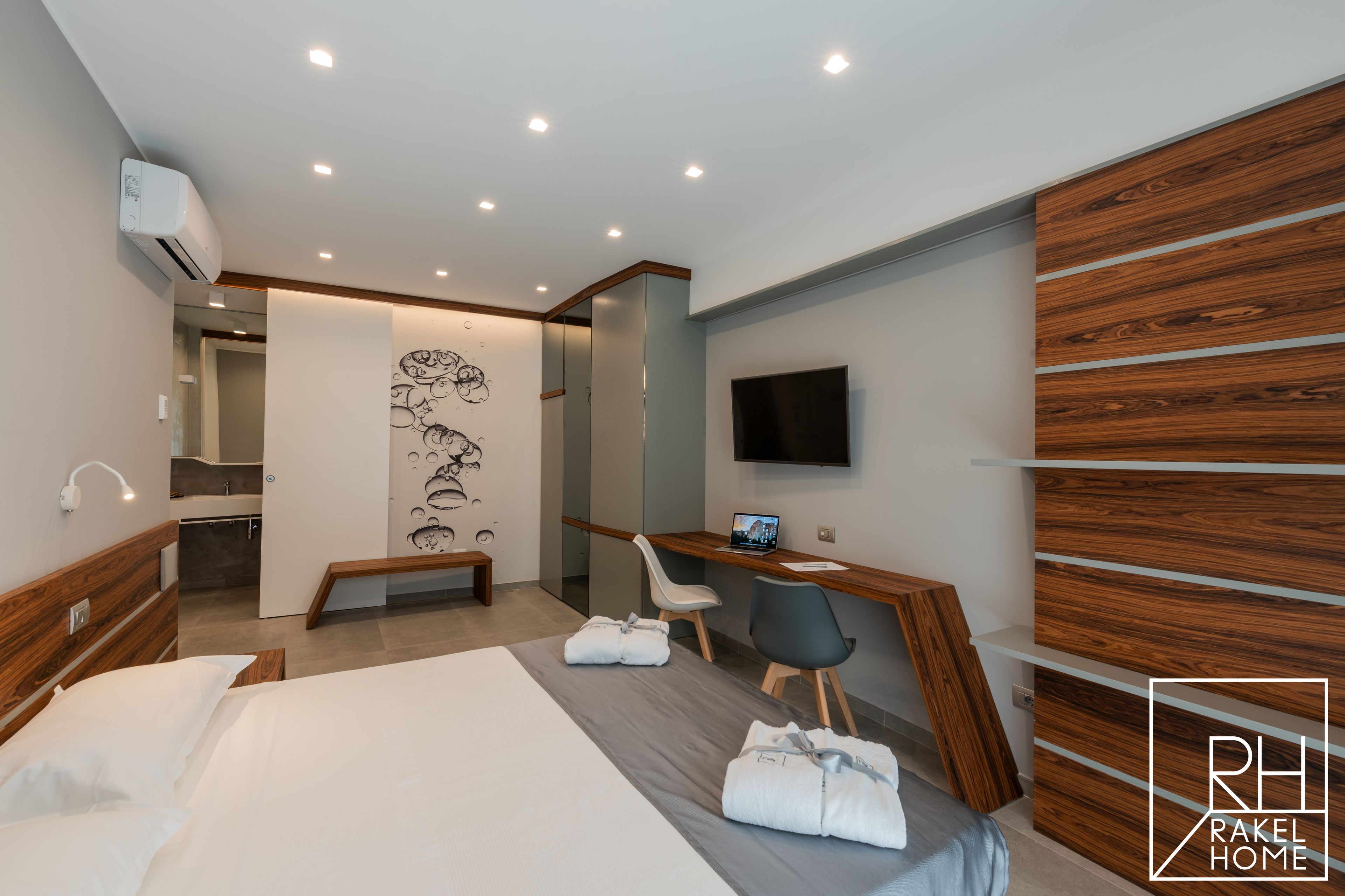 A modern hotel room with a bed, a desk, a chair, a TV, and a wooden accent wall.
