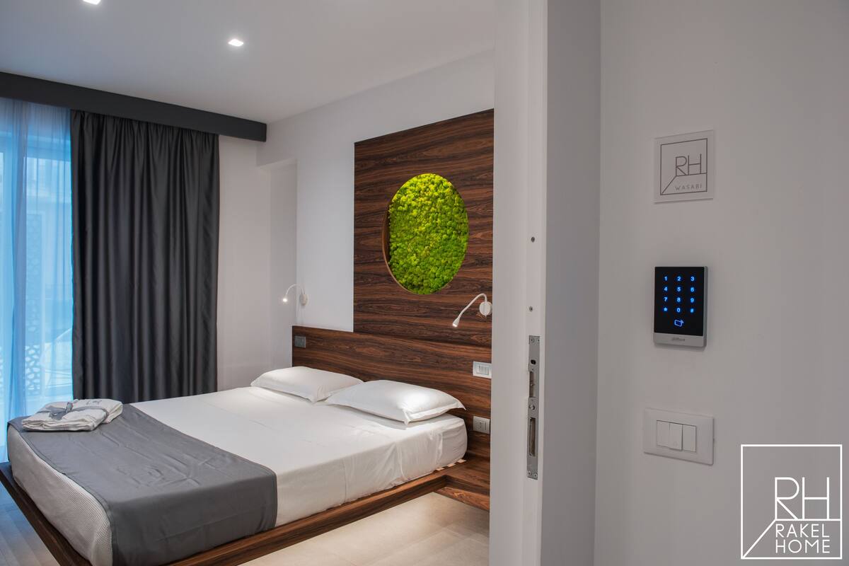 Ein modernes Schlafzimmer mit einem Bett, einer Wandleuchte, einer digitalen Schließanlage und einer grünen Wandgestaltung.