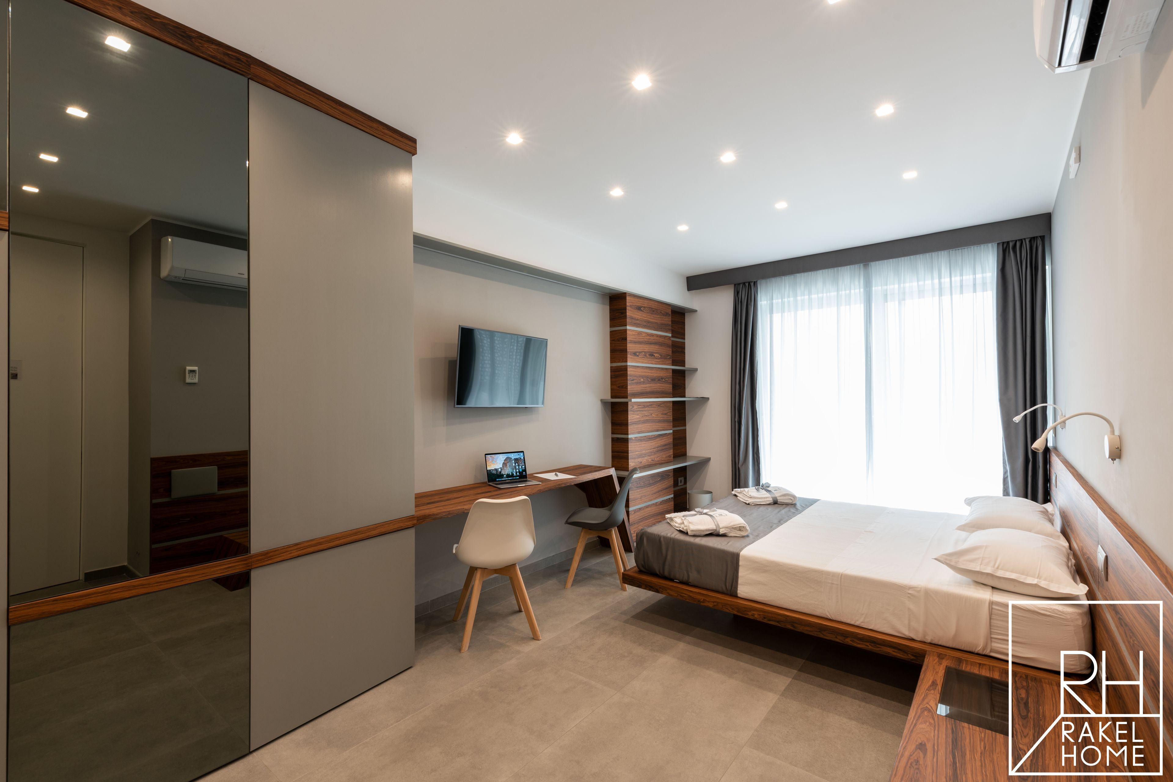A modern hotel room with a bed, desk, chair, and a large mirror.
