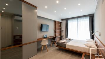 A modern hotel room with a bed, desk, chair, and a large mirror.