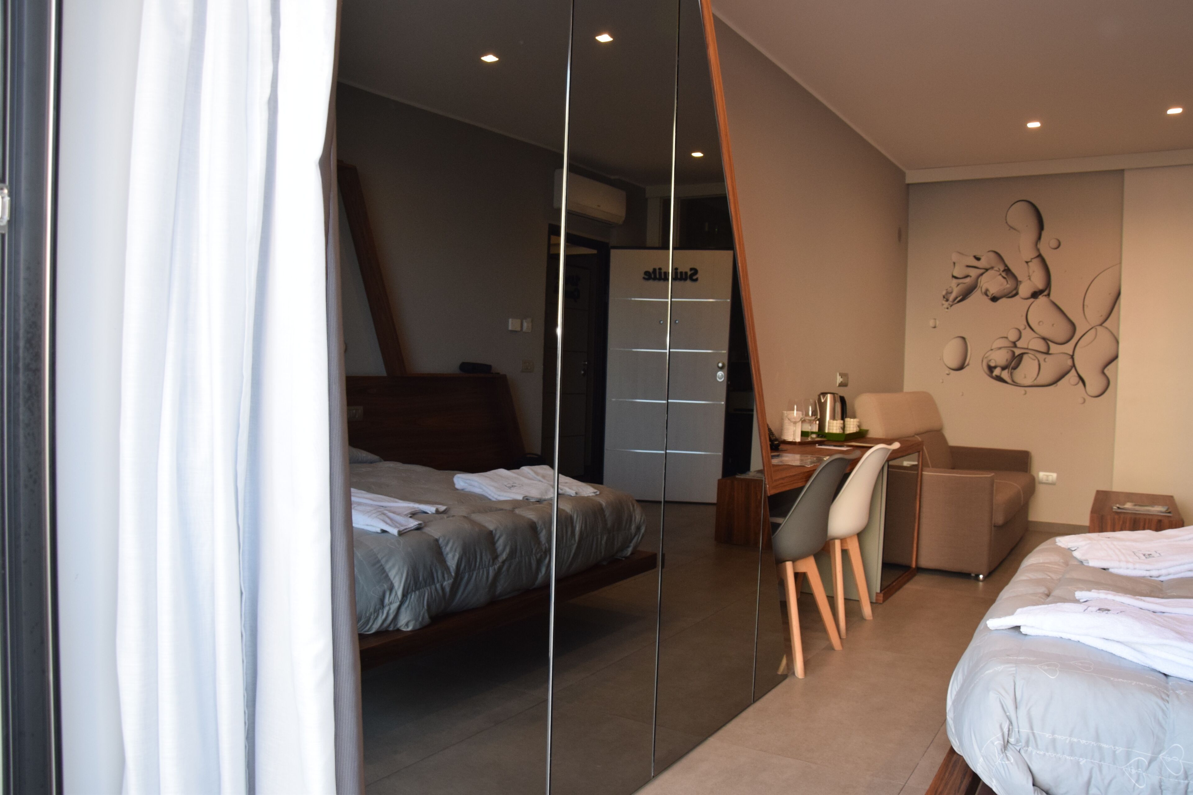 A modern hotel room with a bed, a desk, a chair, and a wardrobe.