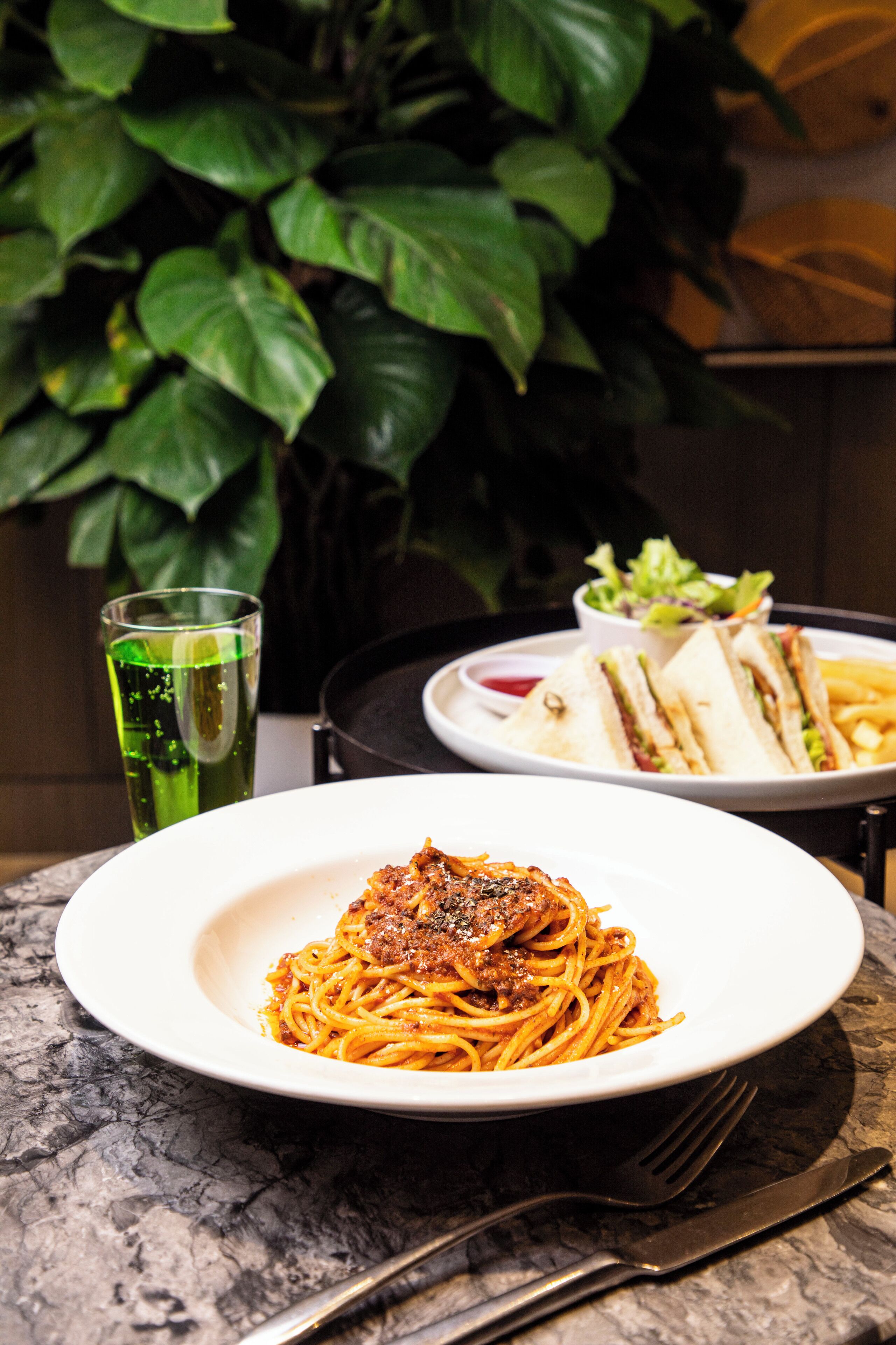 A plate of spaghetti with meat, a sandwich, a salad, and a glass of green drink on a marble table.