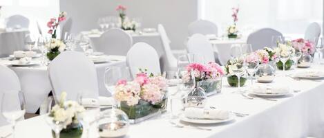 A banquet hall with white tables set for a formal event, each with a floral centerpiece and clear glassware.