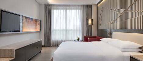 Una habitación de hotel moderna con una cama grande, un televisor montado en la pared, un escritorio y una silla roja.