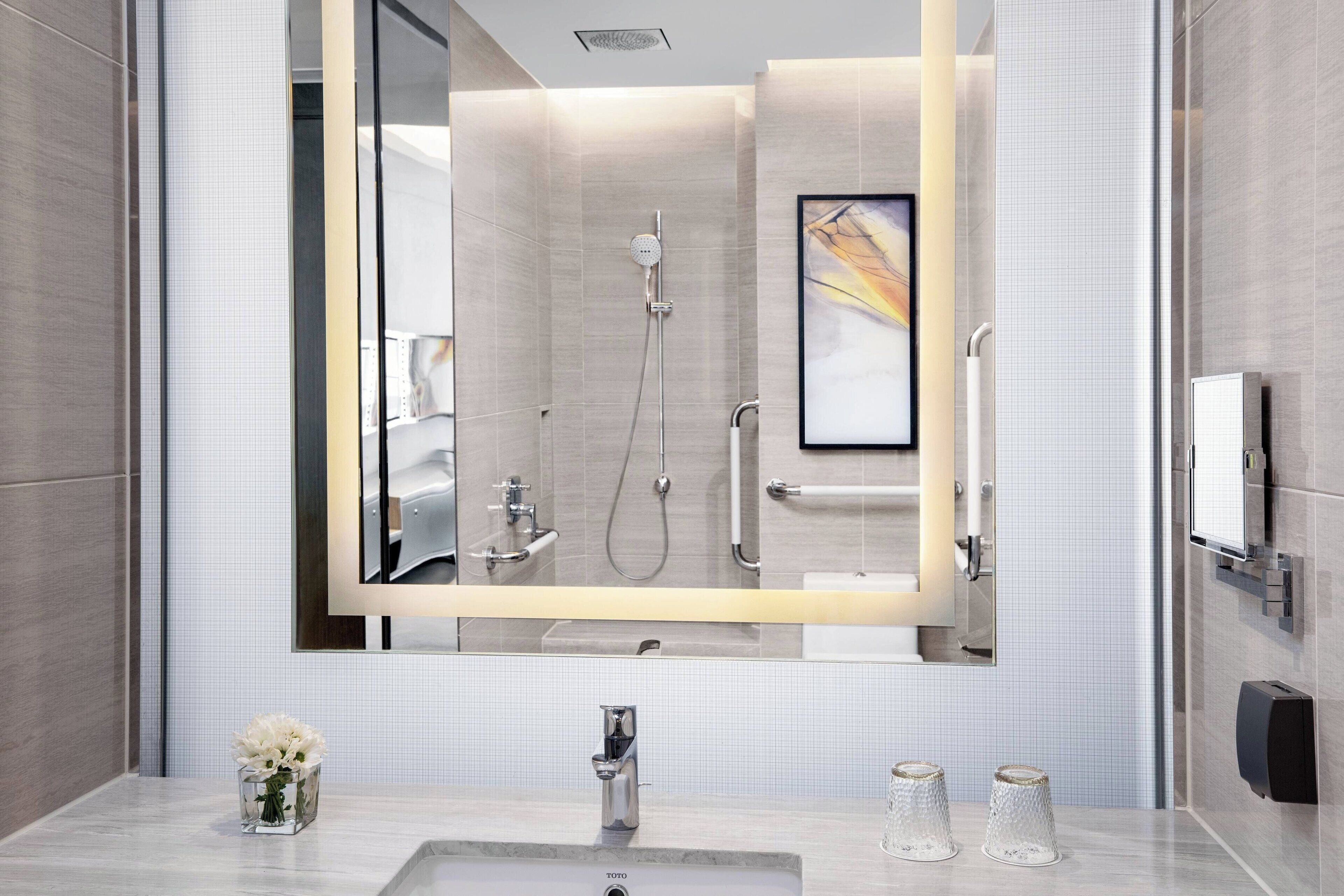 A modern bathroom with a large mirror, a sink, and a shower.