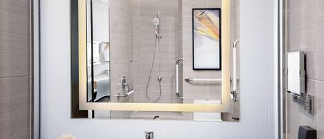 A modern bathroom with a large mirror, a sink, and a shower.