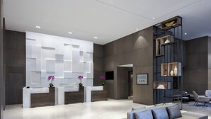 Un hall d’hôtel moderne comprenant un comptoir d’accueil, un espace salon et une grande étagère.