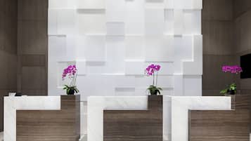 A reception area with three marble counters and wooden panels, each with a potted orchid.