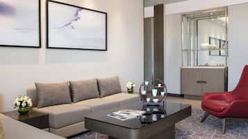 Een moderne woonkamer met een bank, een salontafel en een rode fauteuil. Twee ingelijste kunstwerken hangen aan de muur en een glazen kast met decoratieve objecten.