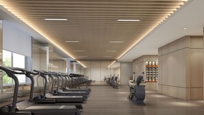 Une salle de sport moderne avec des tapis de course alignés le long du mur, un plafond en bois doté d’un éclairage encastré et une grande fenêtre laissant entrer la lumière naturelle.