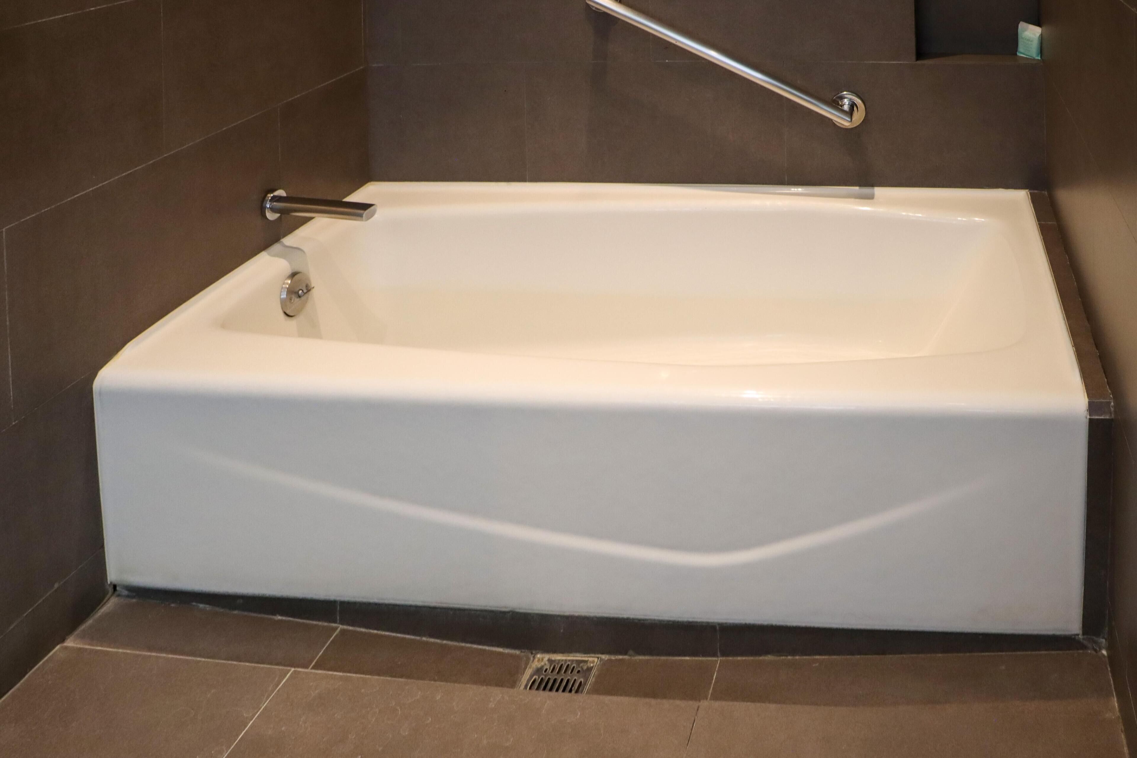 A white bathtub with a chrome faucet and a grab bar, set against a tiled wall.