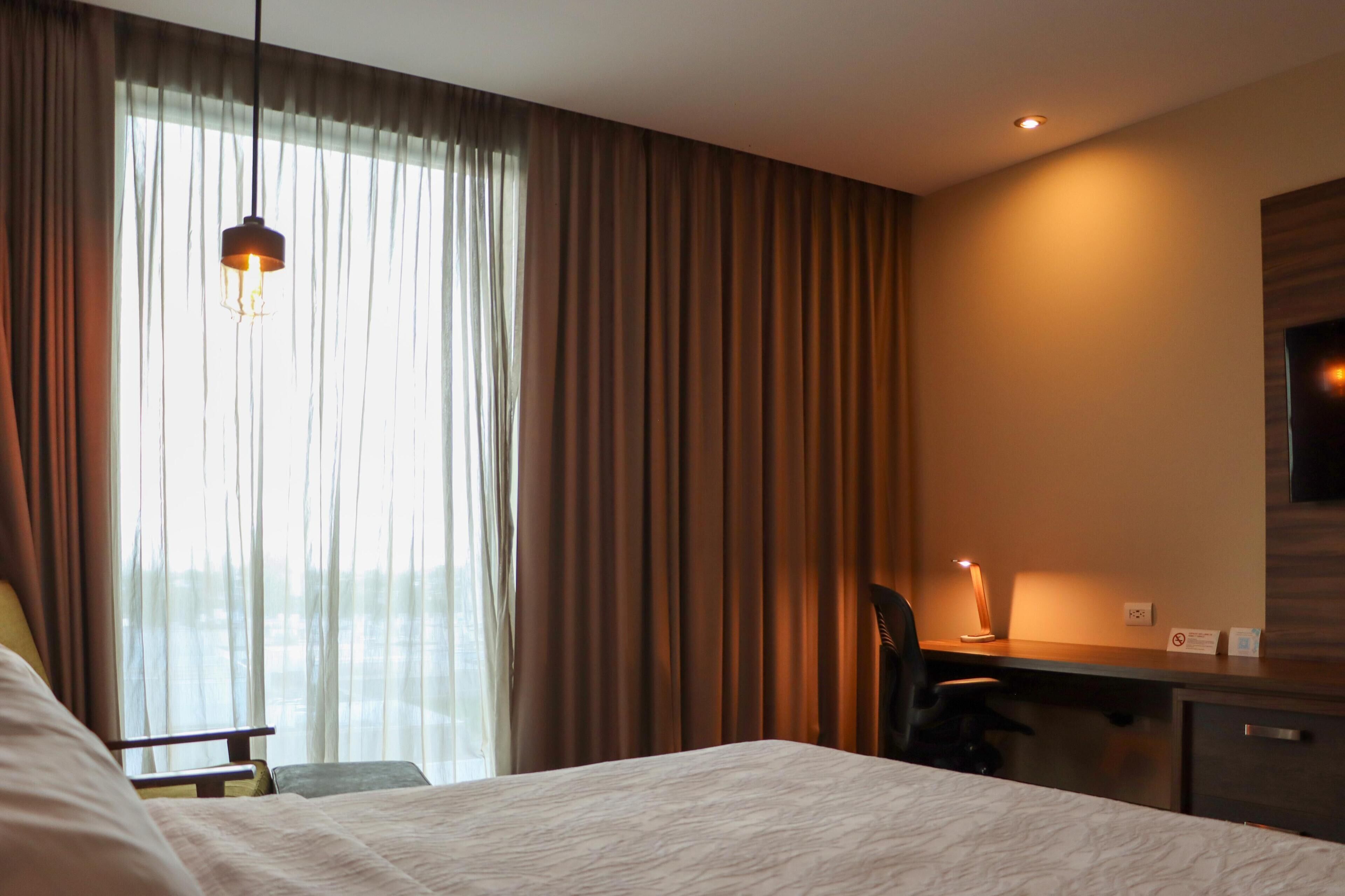 Une chambre d’hôtel avec un lit, un bureau avec une chaise, une lampe de bureau et un téléviseur fixé au mur.