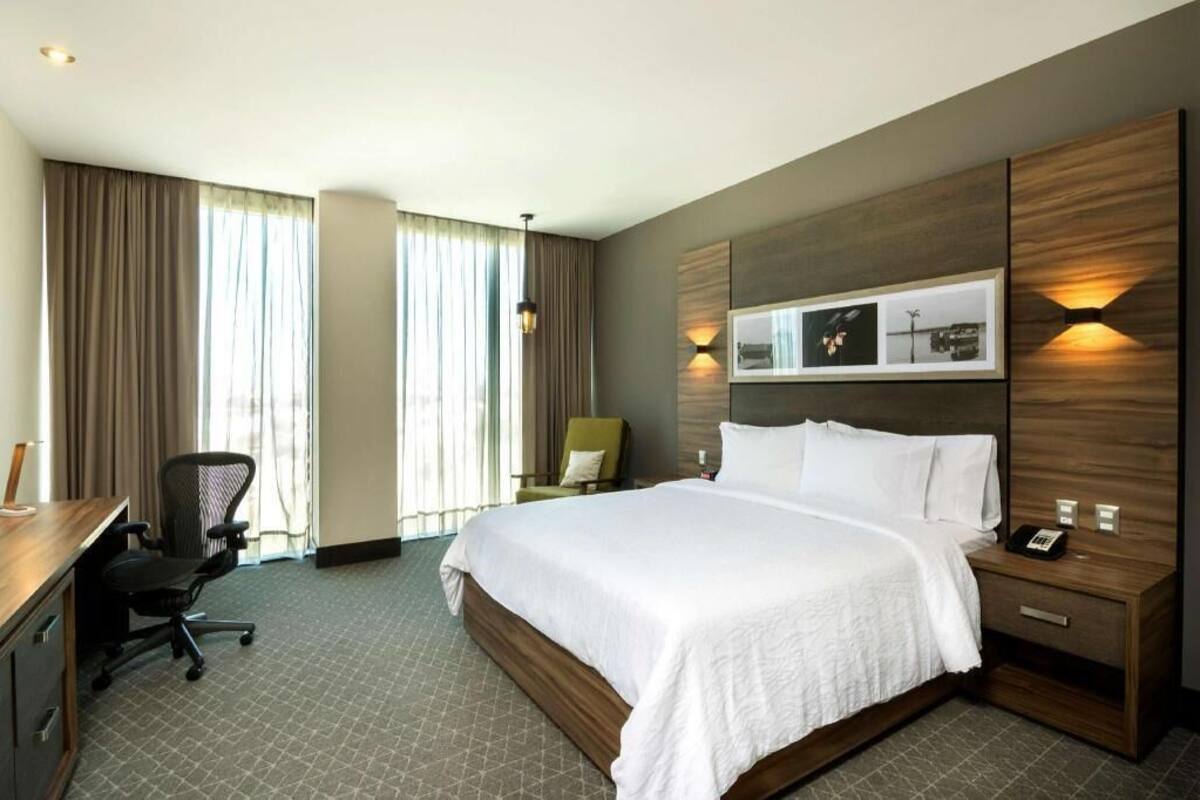 Habitación de hotel con una cama grande, un escritorio, una silla y una lámpara fijada a la pared.