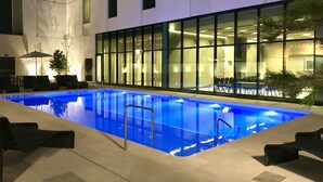 A swimming pool with a glass barrier, lounge chairs, and a seating area with umbrellas. - Hilton Garden Inn Aguascalientes (Aguascalientes)