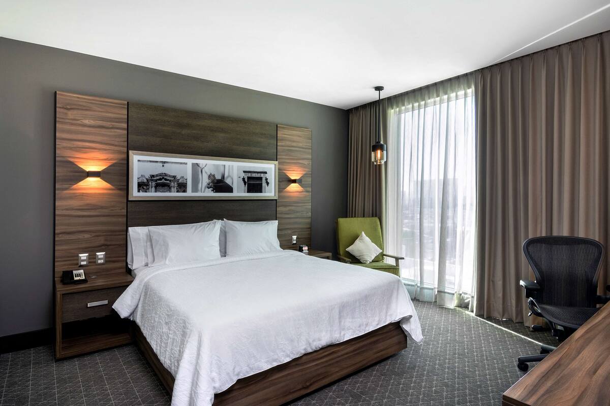 Una habitación de hotel con una cama grande, un escritorio, una silla y una mesita de noche.