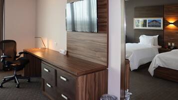 A hotel room with a wooden desk, two beds, a TV, and a framed picture on the wall.