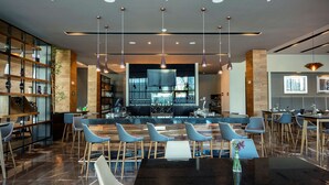 A modern restaurant with a bar area, bar stools, and a mix of seating options including tables and chairs. - Hilton Garden Inn Aguascalientes (Aguascalientes)