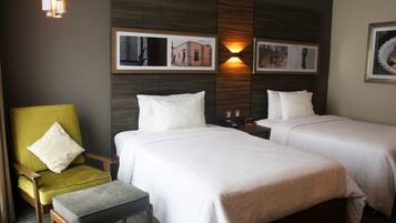A hotel room with two beds, a green armchair, and a small table.