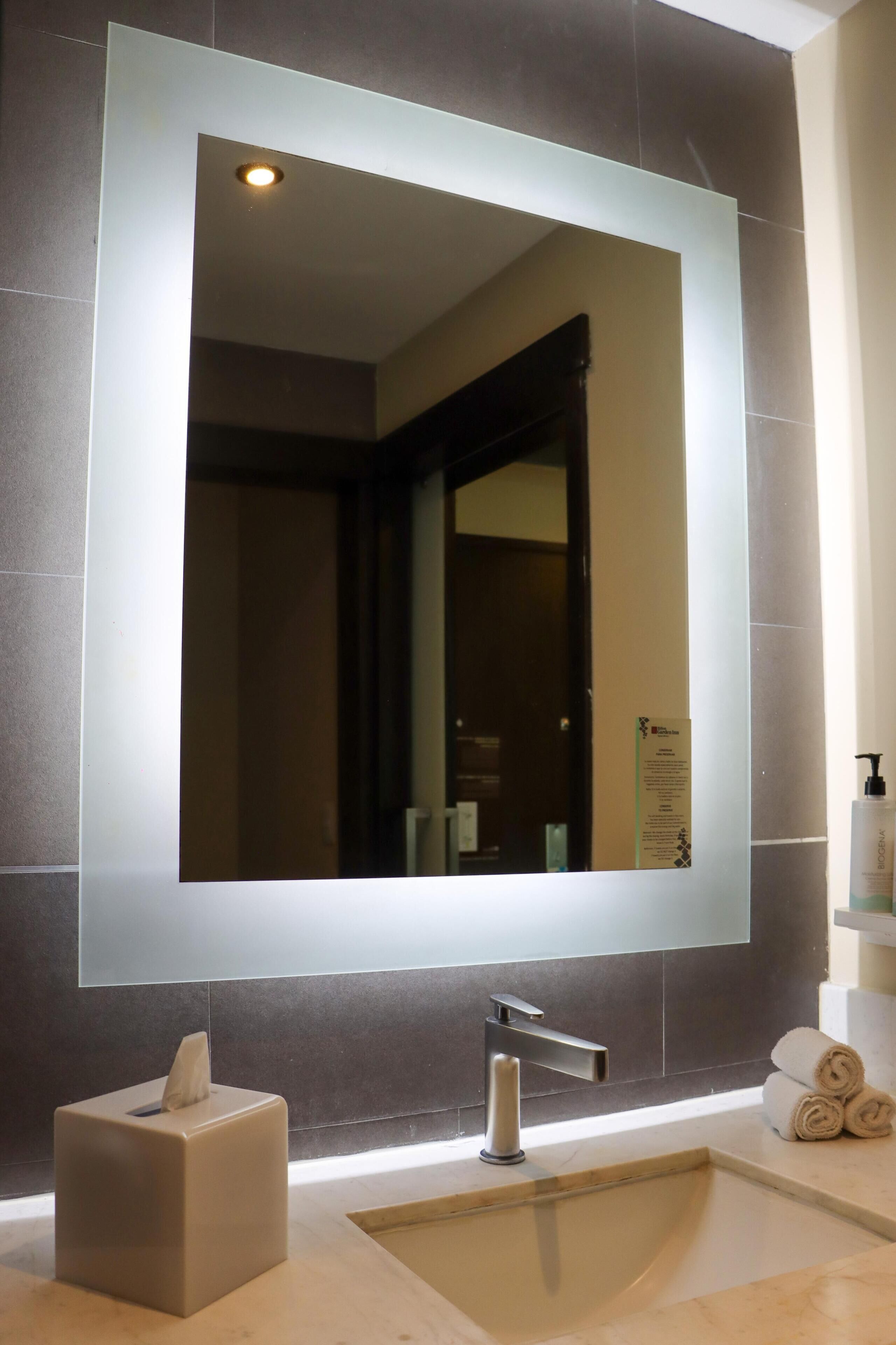 A modern bathroom with a large mirror, a sink, a towel dispenser, and a tissue box.