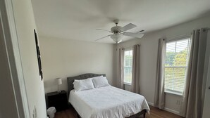 Une chambre à coucher avec un lit, un ventilateur de plafond, une table de chevet et une fenêtre avec des rideaux.