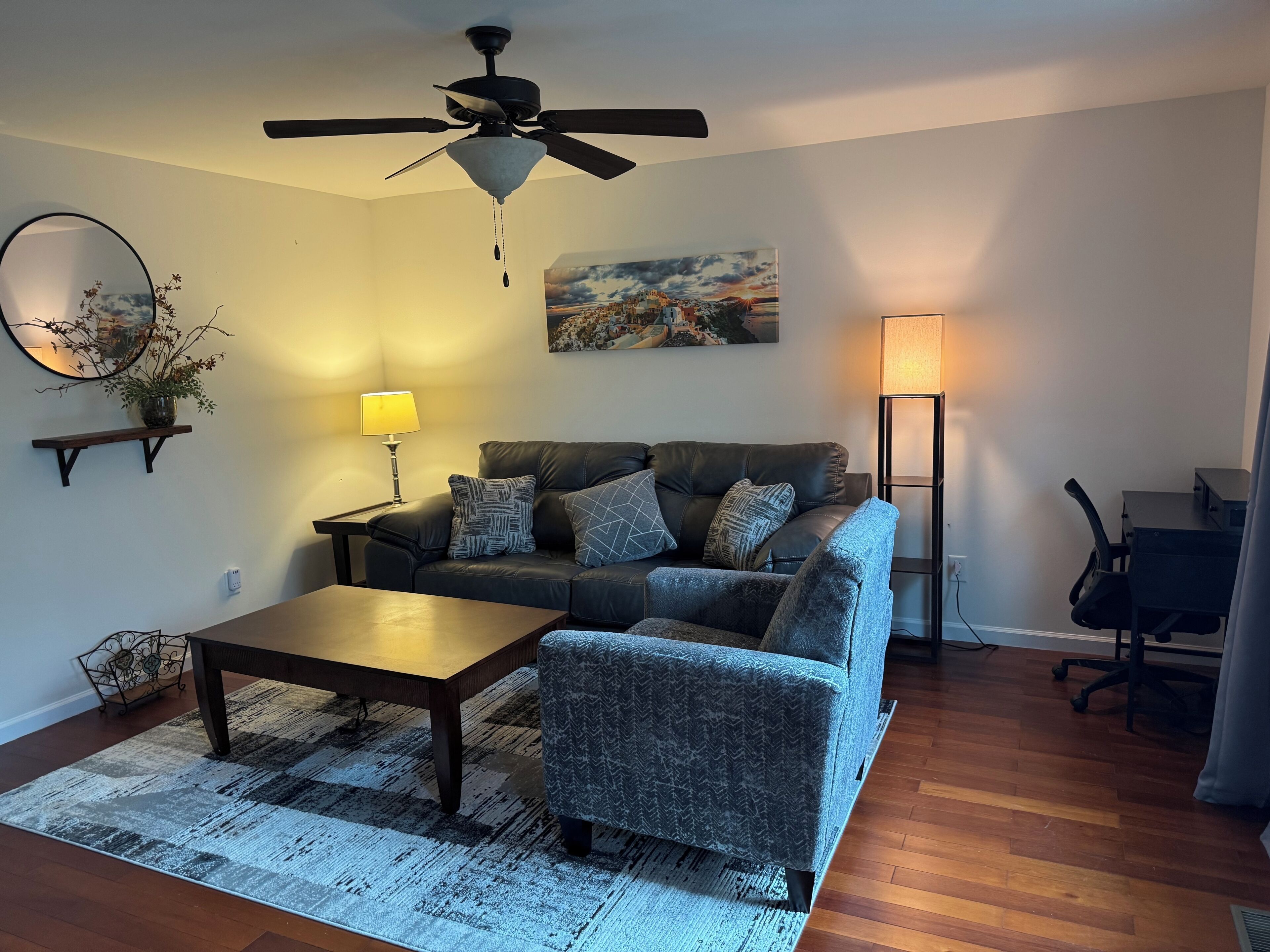 Uma sala de estar com sofá, poltrona, mesa de centro e um quadro na parede.