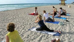 Un grupo de personas practicando yoga en colchonetas sobre la playa.